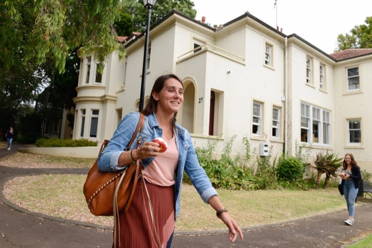 English student eating apple walking in front of English school building